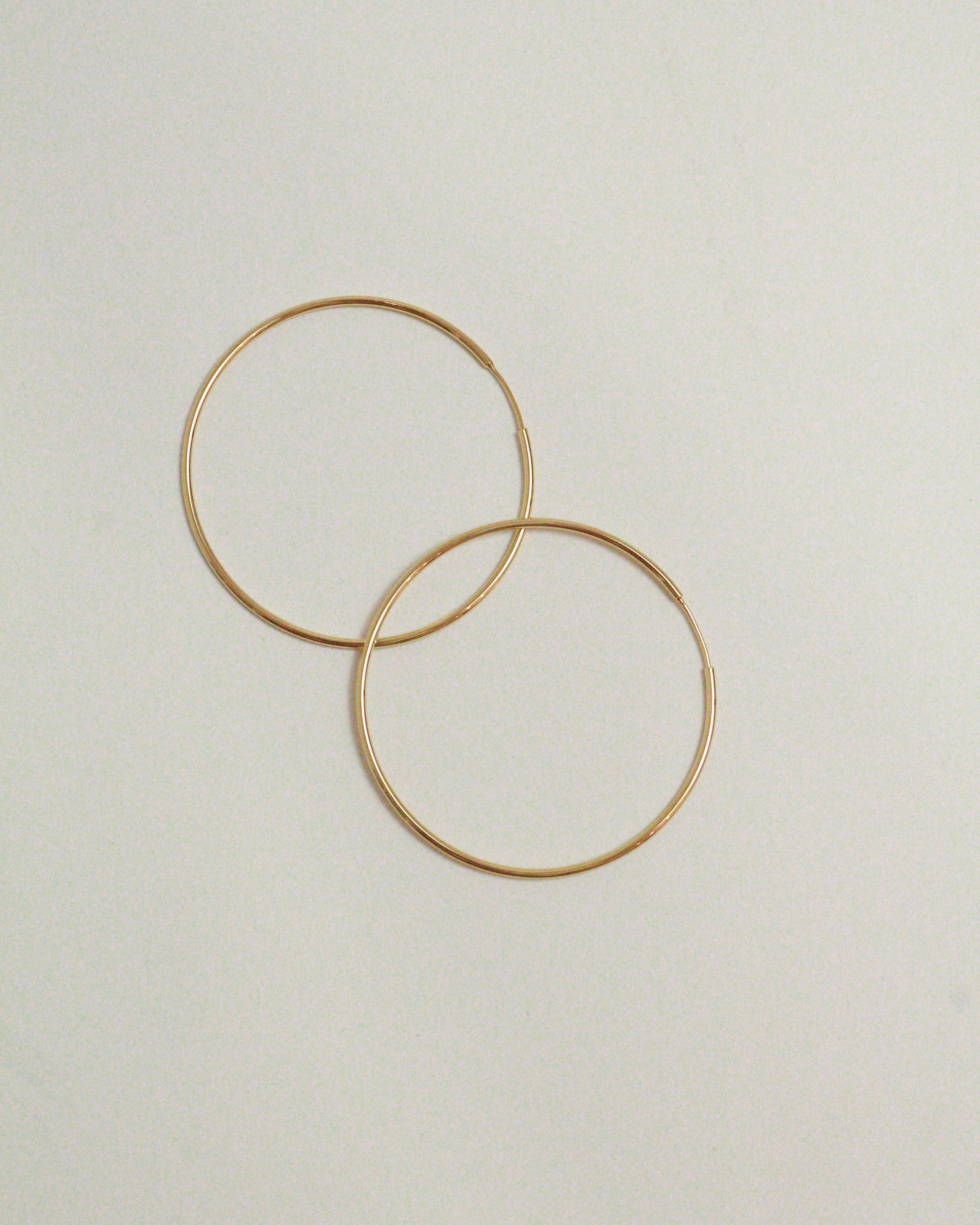 Two gold hoop earrings on a light beige background