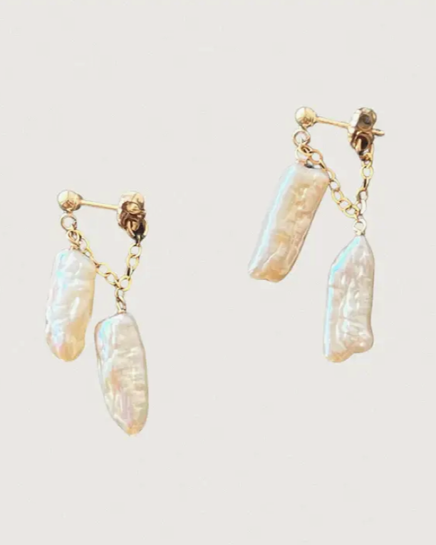 Pair of gold earrings with pearl-like droplets on a light background