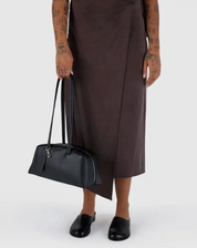 Person holding a black handbag wearing a brown dress on a white background