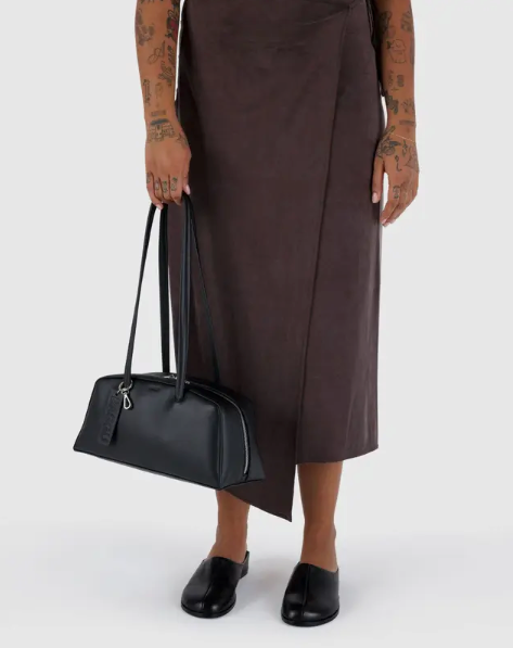 Person holding a black handbag wearing a brown dress on a white background