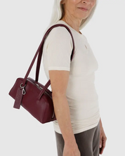 Person holding a maroon recycled leather handbag against a white background