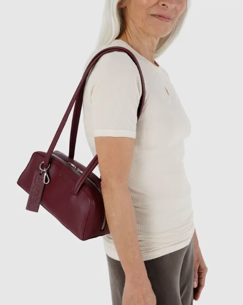 Person holding a maroon recycled leather handbag against a white background