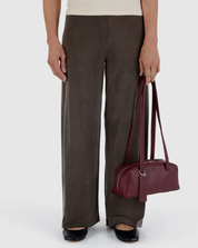 Person wearing brown pants holding a maroon recycled leather handbag on a white background