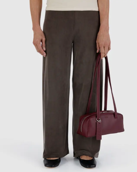Person wearing brown pants holding a maroon recycled leather handbag on a white background