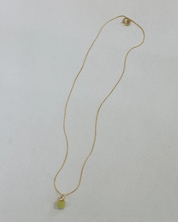 Gold necklace with a green pendant on a light gray background