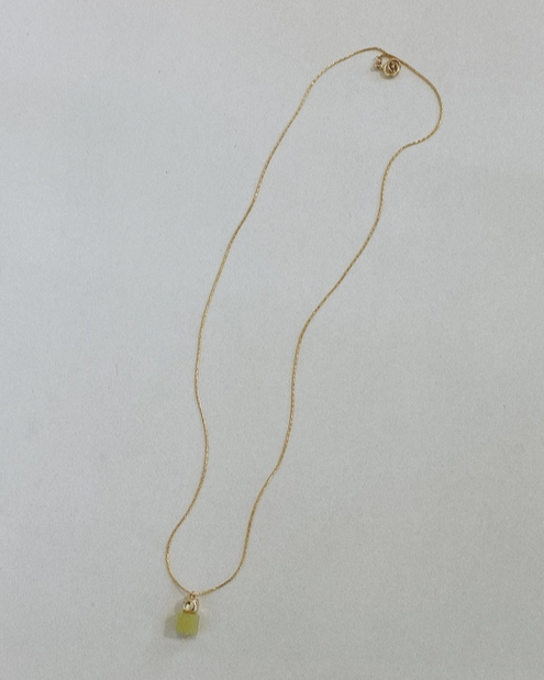 Gold necklace with a green pendant on a light gray background