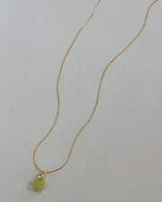 Gold necklace with a small green pendant on a light gray background