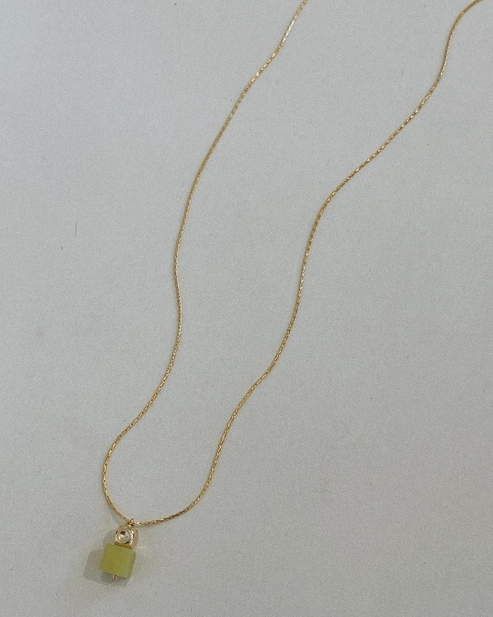 Gold necklace with a small green pendant on a light gray background