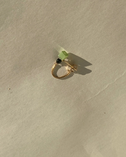 Gold ring with a green stone on a beige surface