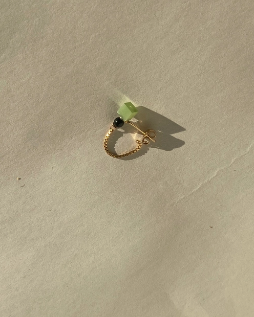 Gold ring with a green stone on a beige surface