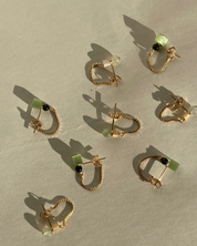 Gold hoop earrings with green and black gemstones on a beige surface