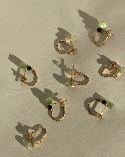 Gold hoop earrings with green and black gemstones on a beige surface