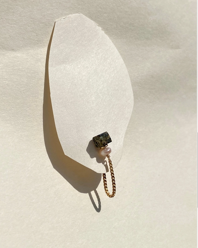 Small decorative item with a chain and gemstone on a textured beige surface