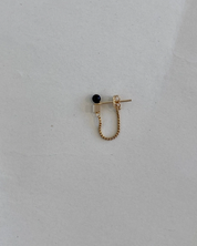 Gold earring with a black bead on a light gray background
