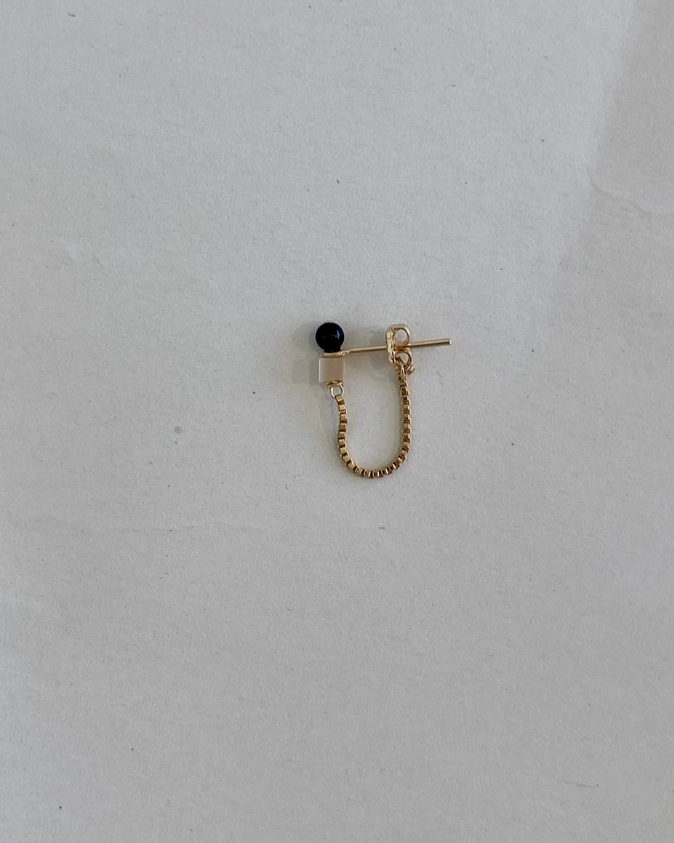 Gold earring with a black bead on a light gray background