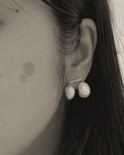 Close-up of an ear wearing a pearl earring with dark hair and skin texture.