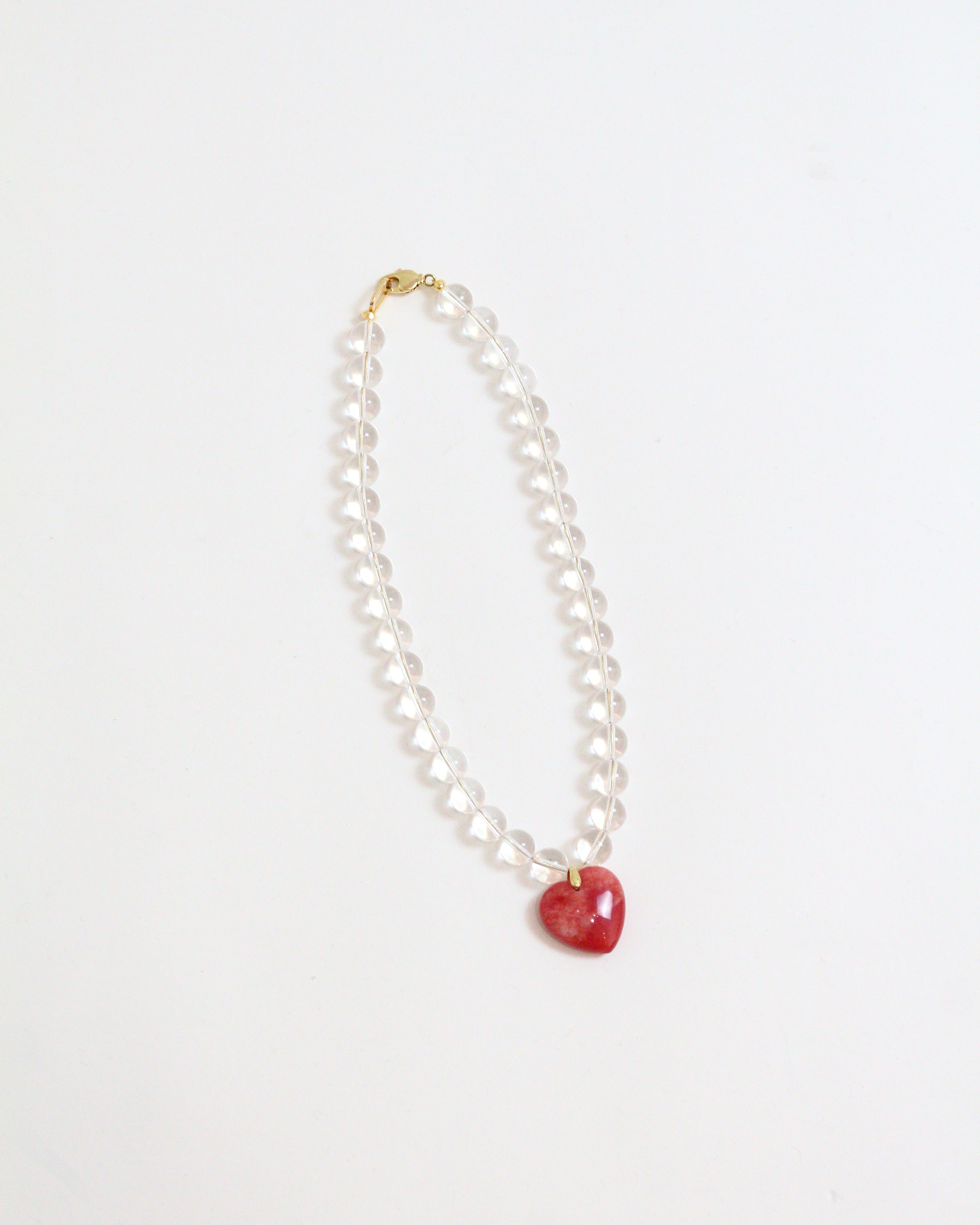 Necklace with a red puffy heart pendant and clear quartz beads on a white background