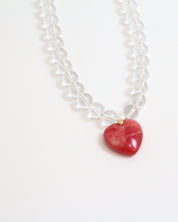 Necklace with a red puffy heart pendant and clear quartz beads on a white background