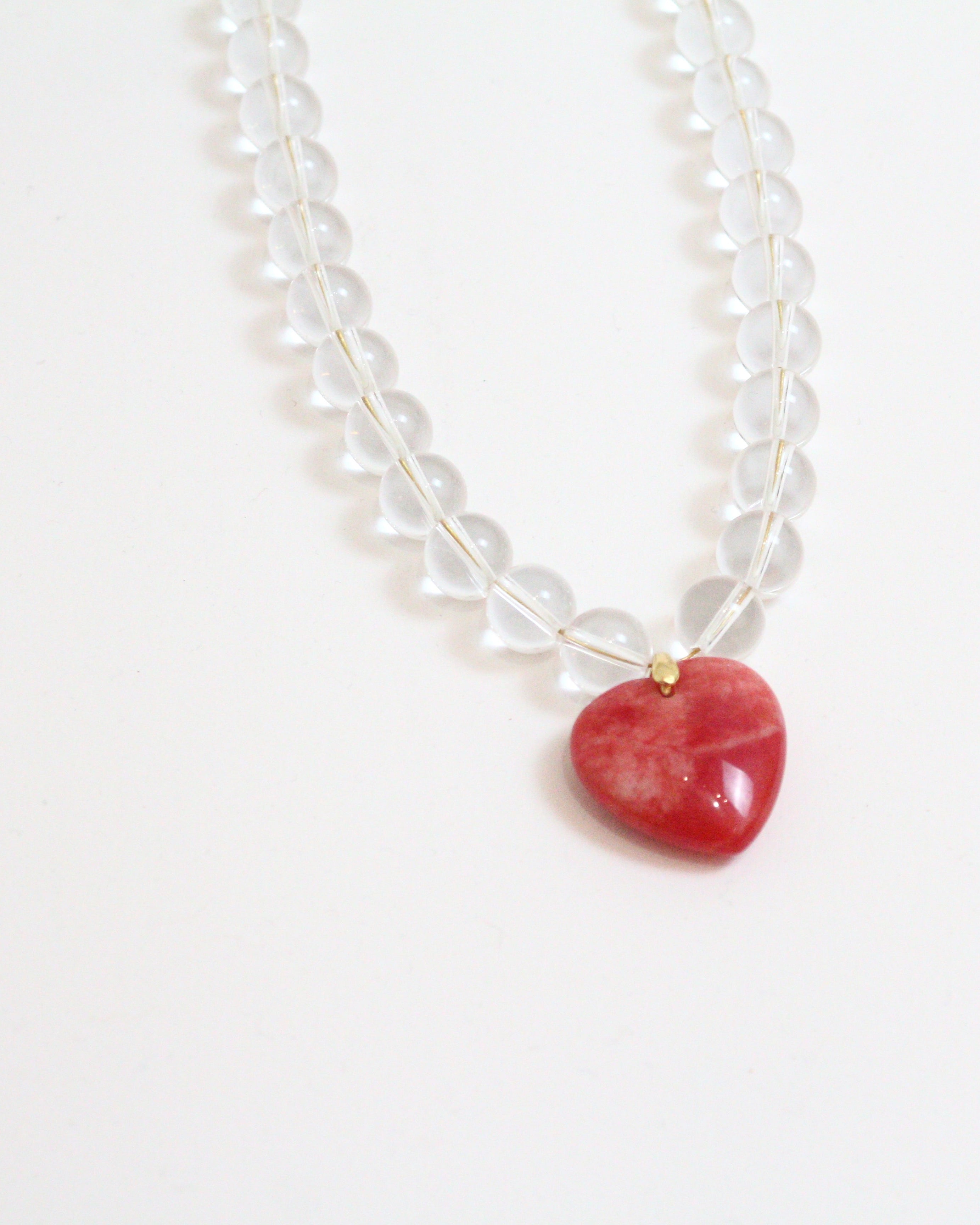 Necklace with a red puffy heart pendant and clear quartz beads on a white background