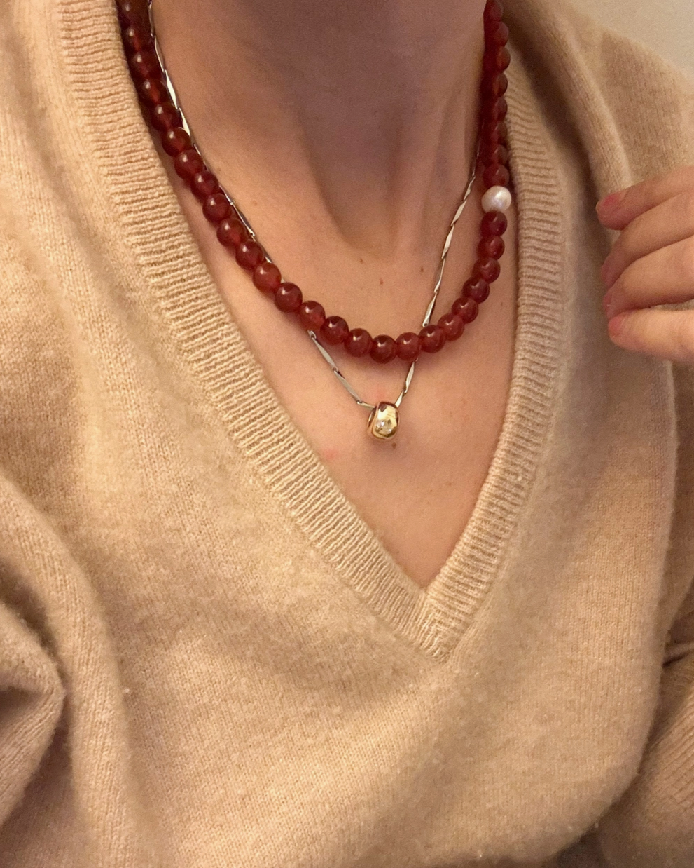 Red carnelian beaded necklace with single fresh water pearl shot on model wearing tan Vneck sweater