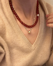 Red carnelian beaded necklace with single fresh water pearl shot on model wearing tan Vneck sweater