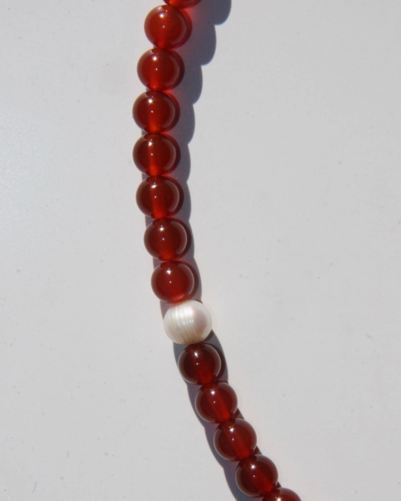 Beaded necklace with red beads and a single white pearl on a light gray background