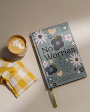 Floral notebook titled 'No Worries' with a cup of coffee and checkered napkin on a beige surface