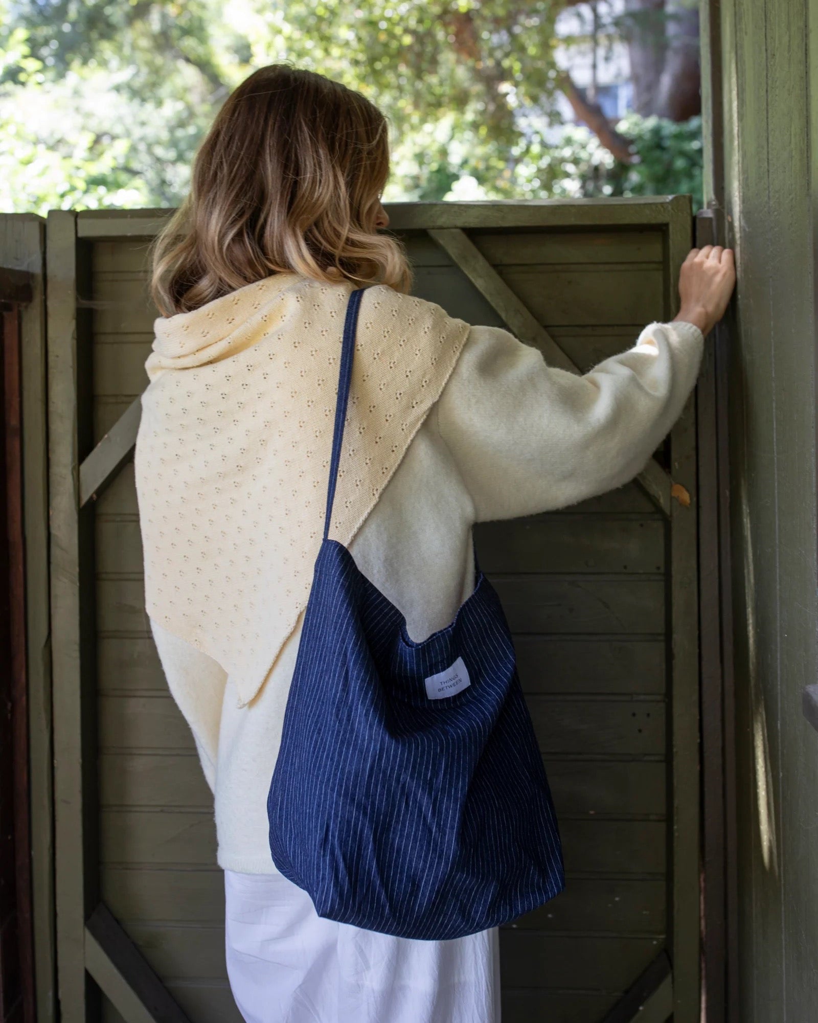 Person with a blue bag standing in front of a wooden door with trees in the background