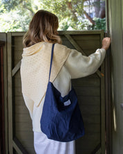Person with a blue bag standing in front of a wooden door with trees in the background