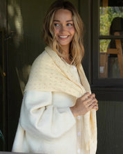 Woman wrapped in a cream-colored shawl standing indoors.