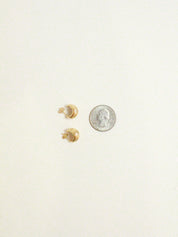 Gold earrings on a white background with a quarter for scale