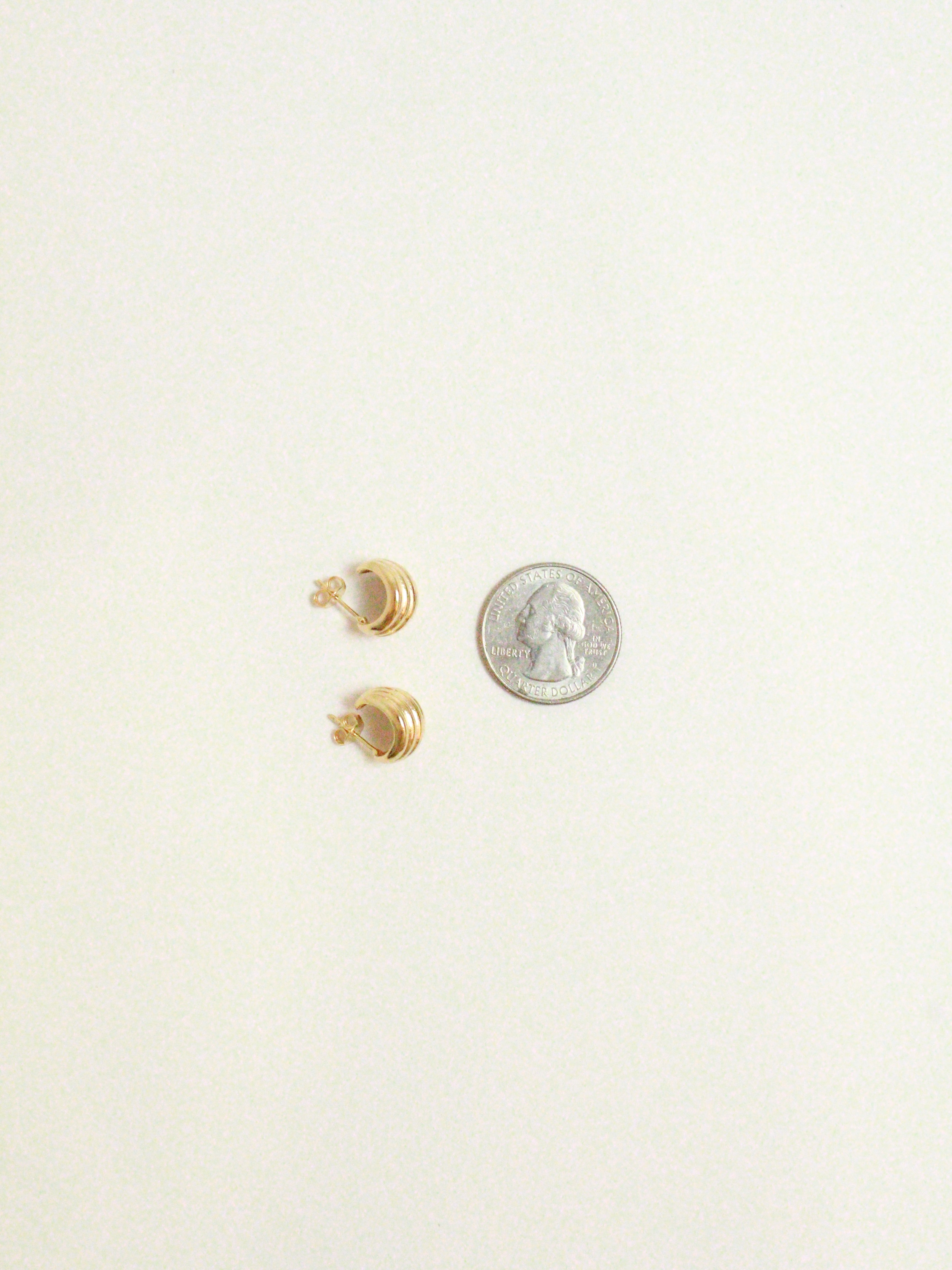 Gold earrings on a white background with a quarter for scale