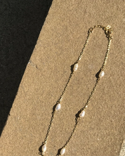 Gold necklace with pearl-like beads on a sandy surface