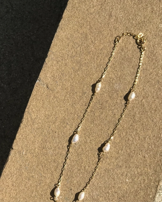 Gold necklace with pearl-like beads on a sandy surface