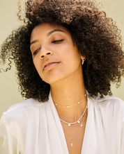 Woman wearing a white blouse and layered necklaces against a neutral background