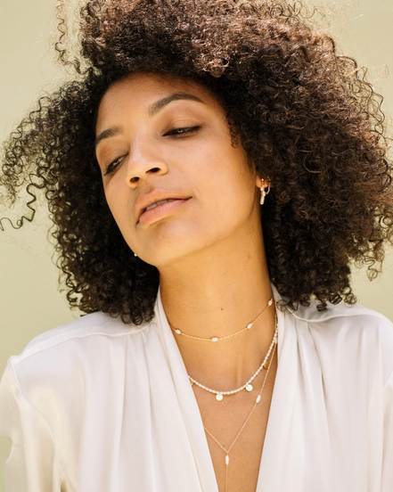 Woman wearing a white blouse and layered necklaces against a neutral background