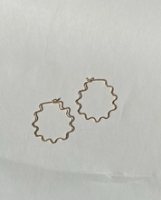 Gold wavy squiggle hoop earrings on a light gray background
