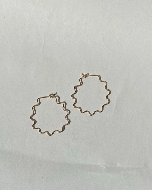 Gold wavy squiggle hoop earrings on a light gray background