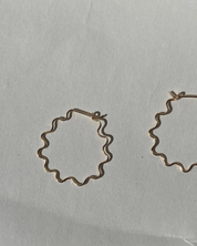 Gold wavy squiggle hoop earrings on a light gray background