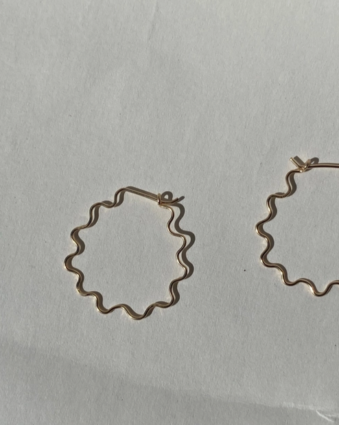 Gold wavy squiggle hoop earrings on a light gray background