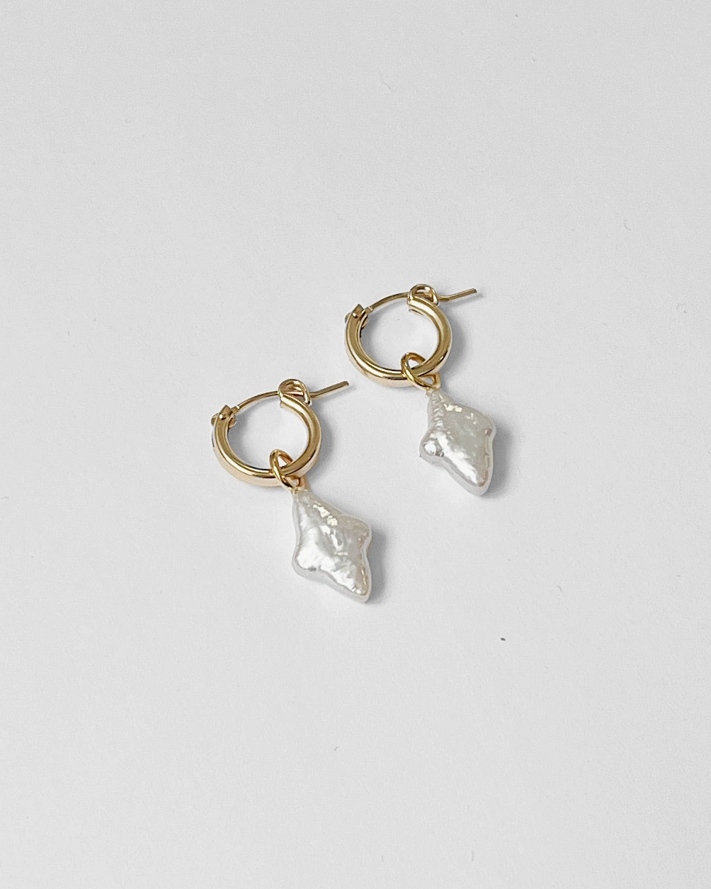 Gold hoop earrings with pearl-like dangling elements on a light gray background