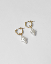 Gold hoop earrings with pearl-like dangling elements on a light gray background