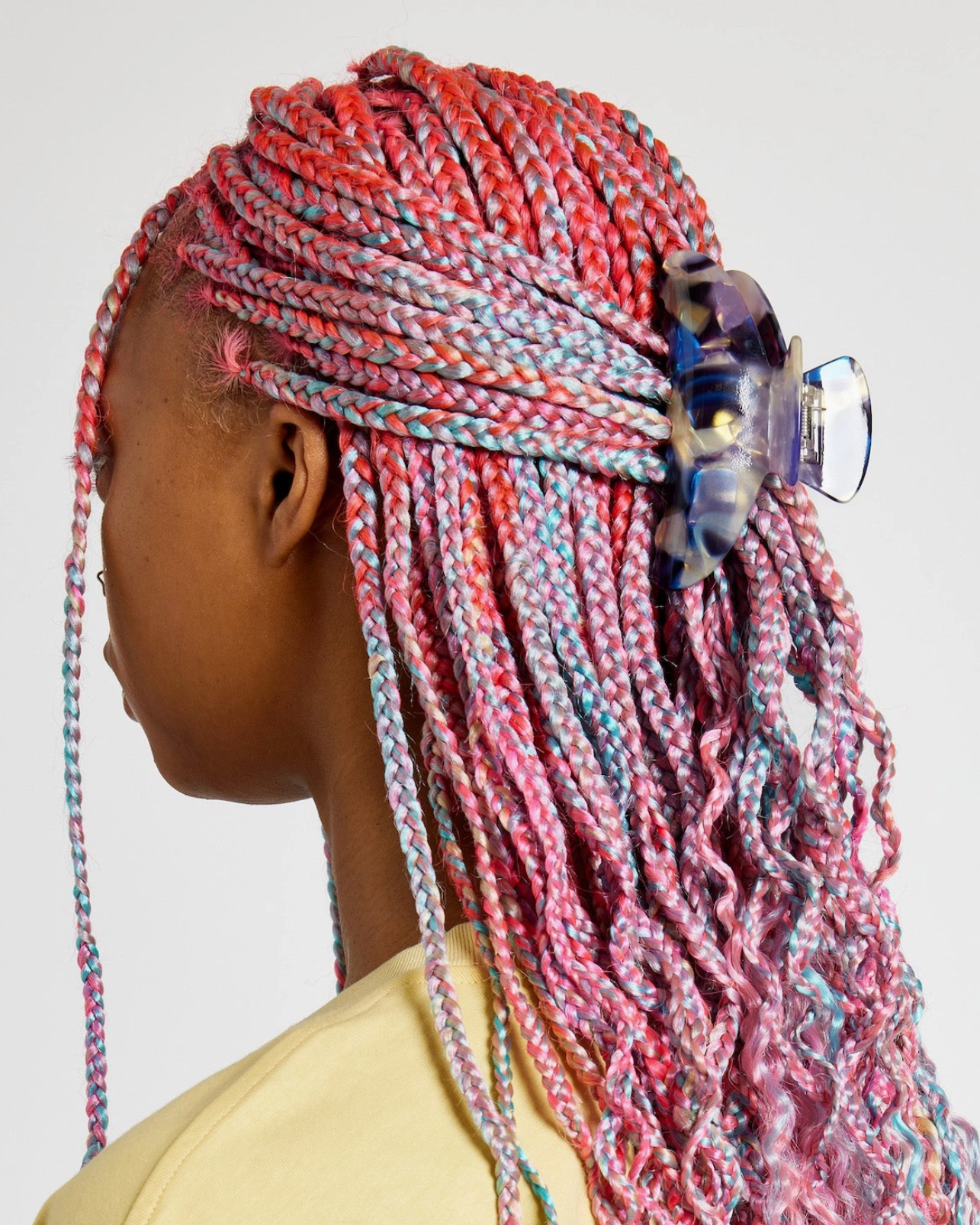 Person with colorful braided hair wearing a yellow top on a plain background