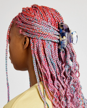 Person with colorful braided hair wearing a yellow top on a plain background