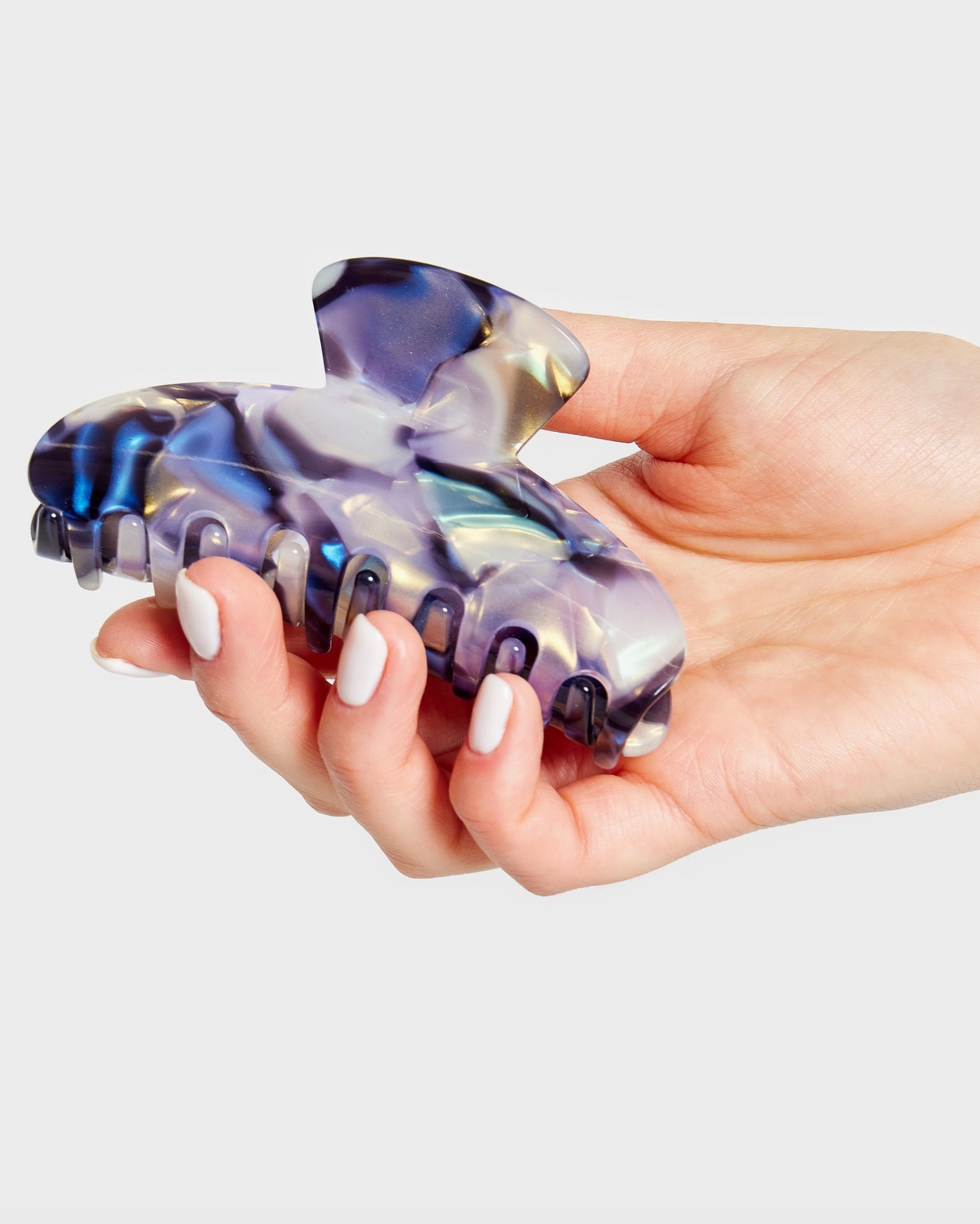 Hand holding a transparent purple and blue hair clip against a light gray background