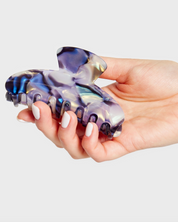 Hand holding a transparent purple and blue hair clip against a light gray background