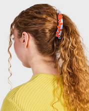 Person with curly hair tied back with a colorful scrunchie on a plain background