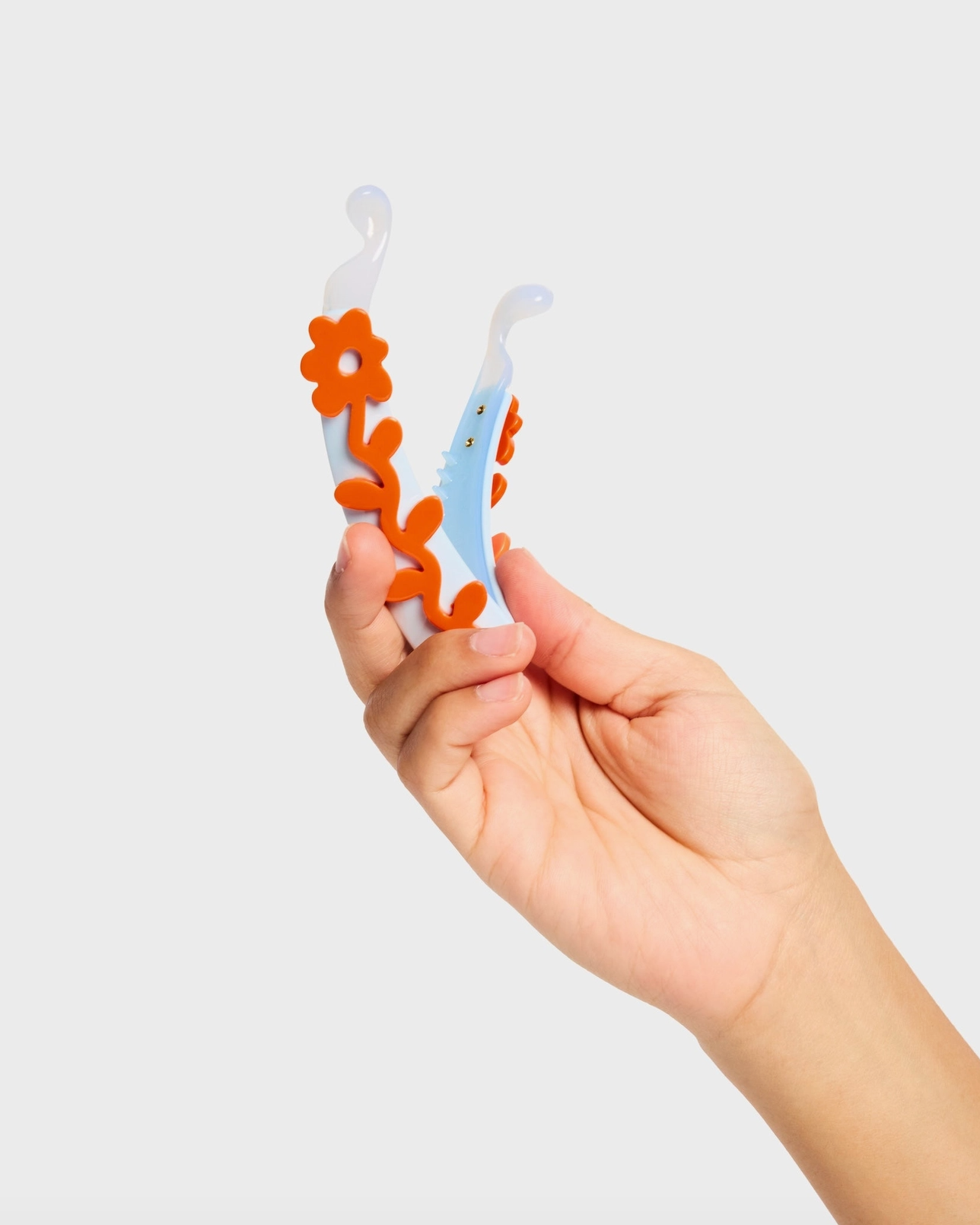 Hand holding a baby teether with floral design against a white background