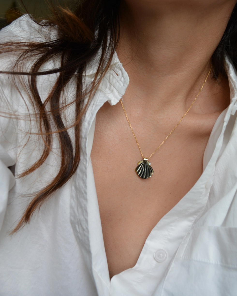 Person wearing a necklace with a shell pendant against a white shirt background