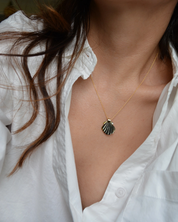 Person wearing a necklace with a shell pendant against a white shirt background